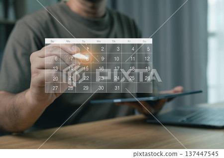 Man marking date on virtual calendar hologram with digital pen, modern schedule and time management concept Man marking date on virtual calendar hologram with digital pen, modern schedule and time management concept 137447545