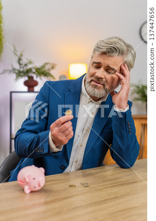 Middle-aged businessman shakes piggy bank counts coins worried about debt bankruptcy planning budget Middle-aged businessman shakes piggy bank counts coins worried about debt bankruptcy planning budget 137447656