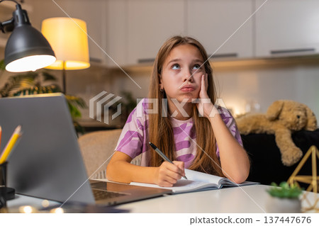 Teenager girl tired with homework writes notes using laptop feels lazy but keeps going with effort Teenager girl tired with homework writes notes using laptop feels lazy but keeps going with effort 137447676