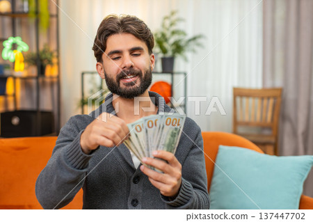 Indian man counts dollar cash banknotes dreams of travel thinks where to spend money smiles wealthy 137447702