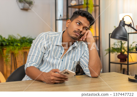 Indian man scrolls smartphone news feed bored frown unhappy tired mood burnout from endless updates Indian man scrolls smartphone news feed bored frown unhappy tired mood burnout from endless updates 137447722