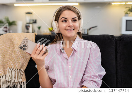 Young woman with wireless headphones nods to music writes idea in smartphone notes and chats online Young woman with wireless headphones nods to music writes idea in smartphone notes and chats online 137447724