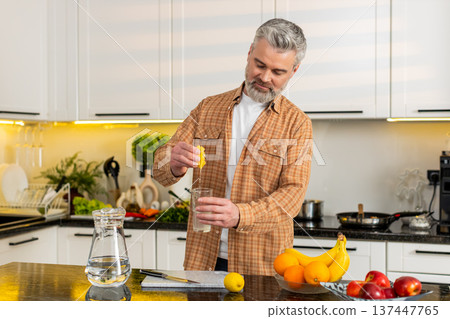Middle-aged man squeezing lemon to make lemonade in kitchen for healthy diet fit hydration lifestyle Middle-aged man squeezing lemon to make lemonade in kitchen for healthy diet fit hydration lifestyle 137447765