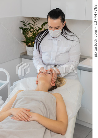 Young woman receiving relaxing facial massage by professional beautician doctor in beauty clinic Young woman receiving relaxing facial massage by professional beautician doctor in beauty clinic 137447768