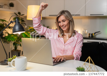 Adult woman receives bonus notification on laptop smiles celebrates raises hand excited jackpot win 137447772