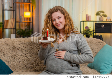 Pregnant woman making birthday wish blowing out cake candle celebrating special home moment Pregnant woman making birthday wish blowing out cake candle celebrating special home moment 137447773