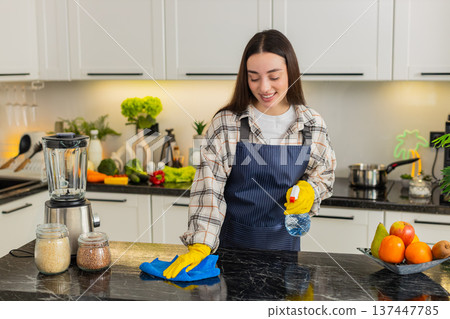 Young woman cleaning kitchen counter with spray and cloth for safe hygiene in home apartment routine Young woman cleaning kitchen counter with spray and cloth for safe hygiene in home apartment routine 137447785
