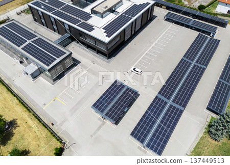 Aerial view of building with solar panels on a roof and parking space with solar canopies. Aerial view of building with solar panels on a roof and parking space with solar canopies. 137449513