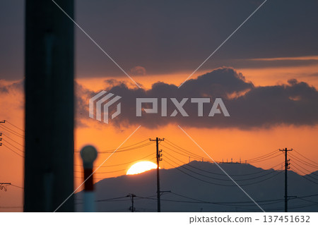 A twilight scene created by the huge sun setting over the mountainside and the silhouette of a series of electric poles A twilight scene created by the huge sun setting over the mountainside and the silhouette of a series of electric poles 137451632