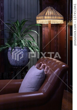 A sanctuary of vintage charm, this corner features a supple leather club chair that invites quiet reflection, accompanied by a soft lavender pillow. A floor lamp, crowned with a fringed, 137451941