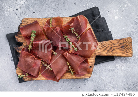 Dried beef meat Cecina, slices of beef jerky on wooden board with herbs. grey background. top view Dried beef meat Cecina, slices of beef jerky on wooden board with herbs. grey background. top view 137454490