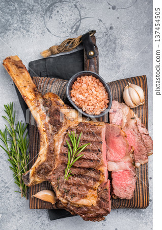BBQ fried Tomahawk beef steak, grilled marbled rib eye with bone on wooden board. grey background. top view BBQ fried Tomahawk beef steak, grilled marbled rib eye with bone on wooden board. grey background. top view 137454505