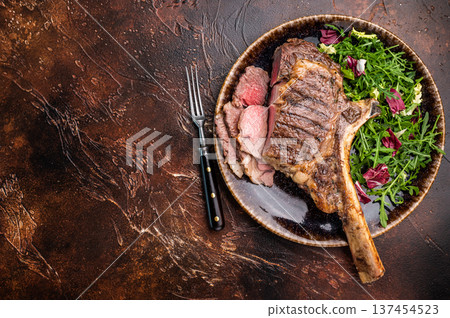 Grilled and sliced Tomahawk beef steak, marble rib eye with bone on plate with salad. brown background. top view Grilled and sliced Tomahawk beef steak, marble rib eye with bone on plate with salad. brown background. top view 137454523