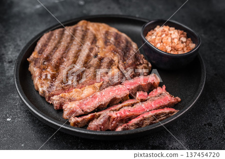Grilled ribeye beef steak sliced and served in plate with herbs. Juicy marbled cooked rib fillet meat on dark stone background. 137454720