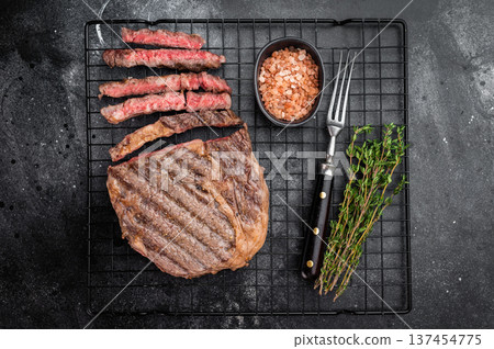 Medium rare rib eye steak sliced and rested on rack with thyme and salt. Premium grilled rib fillet beef in rustic food styling. Medium rare rib eye steak sliced and rested on rack with thyme and salt. Premium grilled rib fillet beef in rustic food styling. 137454775