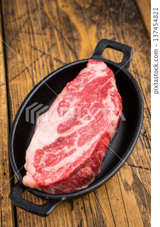 Fresh raw beef chuck eye roll cut in skillet with herbs on wood background. Beef meat ingredient overhead with copy space. Fresh raw beef chuck eye roll cut in skillet with herbs on wood background. Beef meat ingredient overhead with copy space. 137454821