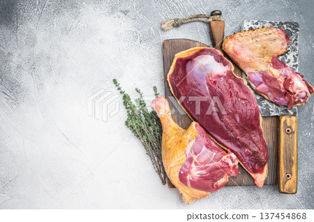 Raw duck meat cuts with breast and leg on wooden board with knife and thyme. Gamebird poultry game meat on gray background copy space. Raw duck meat cuts with breast and leg on wooden board with knife and thyme. Gamebird poultry game meat on gray background copy space. 137454868