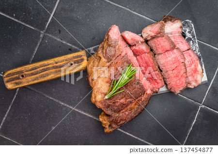 Grilled and Sliced beef chuck eye roll steak cooked medium rare on meat cleaver with rosemary on dark tile background with copy space. Grilled and Sliced beef chuck eye roll steak cooked medium rare on meat cleaver with rosemary on dark tile background with copy space. 137454877