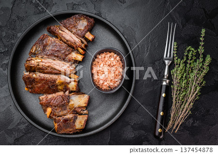 Sliced BBQ roasted lamb breast ribs on black plate with salt and fork dark stone background barbecue meat copy space. 137454878