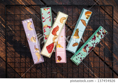 Variety of handmade gourmet chocolate bars with berry and nut toppings on metal grid dark wood backdrop luxury sweets 137454926