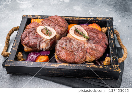 Flavorful ossobuco garnished with fresh herbs, osso buco shank ideal for impressing guests at your next dinner party. grey background. top view Flavorful ossobuco garnished with fresh herbs, osso buco shank ideal for impressing guests at your next dinner party. grey background. top view 137455035