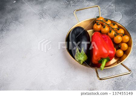 Fresh vegetables in golden pan on light textured background with copy space, red pepper eggplant and yellow cherry tomatoes 137455149