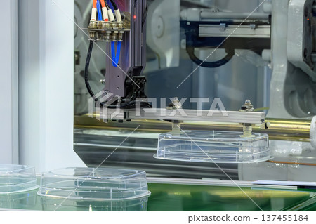 Industrial robotic arm with a pneumatic gripper performing precise pick-and-place of injection-molded plastic parts onto a conveyor belt. 137455184