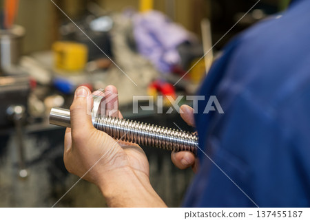 Machine operator performing a functional assembly check on precision-turned parts using a matching nut to verify thread fit and dimensional tolerance. 137455187