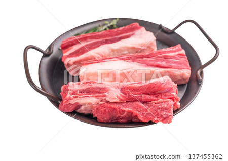 Raw bone-in beef short ribs ready for cooking, garnished with rosemary sprigs on a dark metal platter. Raw bone-in beef short ribs ready for cooking, garnished with rosemary sprigs on a dark metal platter. 137455362