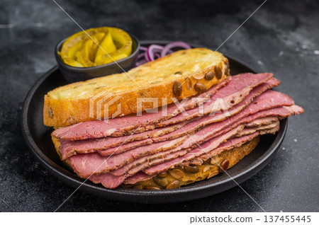Smoked pastrami brisket slices in a hearty sandwich with seed crusted bread, onions and pickles on dark stone surface. Smoked pastrami brisket slices in a hearty sandwich with seed crusted bread, onions and pickles on dark stone surface. 137455445