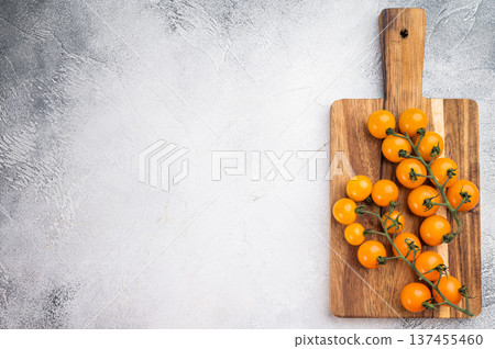 Yellow cherry tomatoes on vine on wooden cutting board over light textured background with copy space, fresh organic produce Yellow cherry tomatoes on vine on wooden cutting board over light textured background with copy space, fresh organic produce 137455460