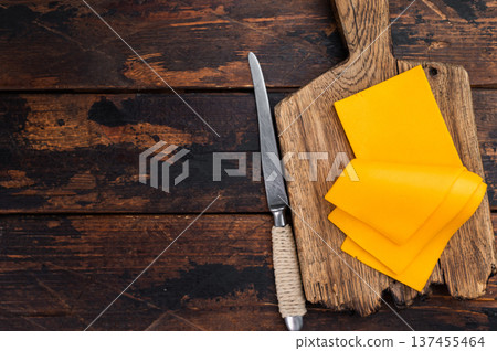 Sliced cheddar style cheese on wooden cutting board with knife over rustic table background and copy space for food design Sliced cheddar style cheese on wooden cutting board with knife over rustic table background and copy space for food design 137455464