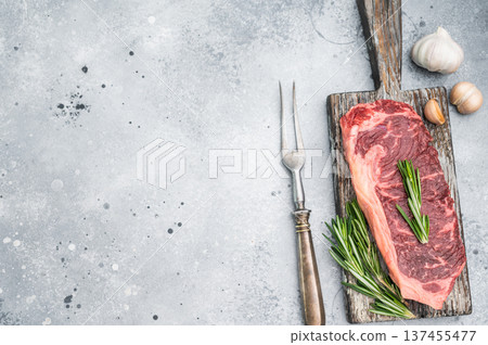 Premium New York steak raw and marbled with rosemary placed on rustic board on bright stone background great for gourmet cooking concepts 137455477
