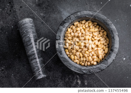 Raw pine nuts placed in a grey stone mortar on a deep textured black backdrop creating a bold rustic look perfect for culinary stock content Raw pine nuts placed in a grey stone mortar on a deep textured black backdrop creating a bold rustic look perfect for culinary stock content 137455496