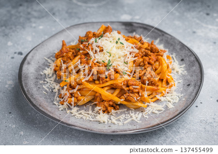 Hearty Italian bolognese pasta topped with minced meat sauce and grated cheese on a gray ceramic plate against stone background. Hearty Italian bolognese pasta topped with minced meat sauce and grated cheese on a gray ceramic plate against stone background. 137455499