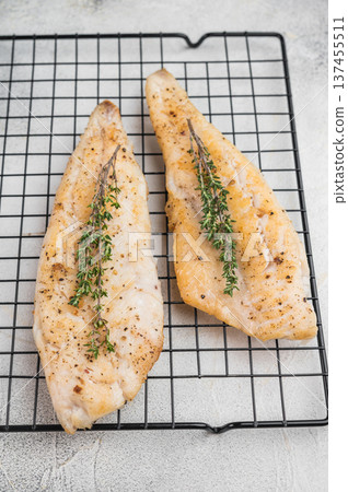Roasted flaky whitefish fillets with fresh thyme, food photography on cooling rack over light stone background. 137455511