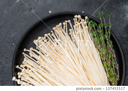 Styled flat lay: Enoki mushrooms, fresh thyme, and garlic on a black plate against a dark, dramatic stone background. Styled flat lay: Enoki mushrooms, fresh thyme, and garlic on a black plate against a dark, dramatic stone background. 137455517