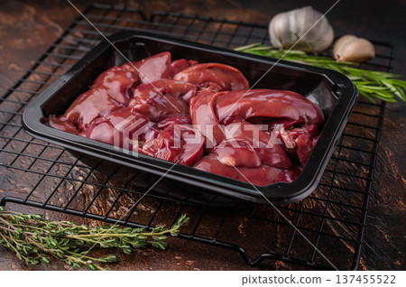 Raw turkey liver in a black tray, surrounded by garlic and fresh herbs, set against a rustic dark background. Raw turkey liver in a black tray, surrounded by garlic and fresh herbs, set against a rustic dark background. 137455522