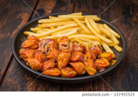 Sliced currywurst, wurst in curry sauce with crispy pommes on dark wood surface ideal for restaurant menus comfort food ads and culinary content. 137455525