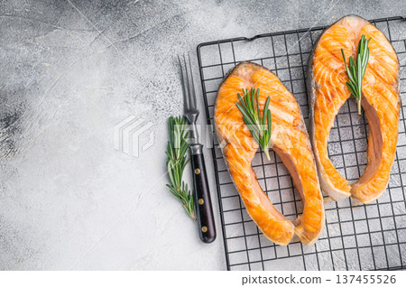 Grilled salmon steaks with rosemary on a black rack over a light textured background creating a bright rustic culinary composition. Grilled salmon steaks with rosemary on a black rack over a light textured background creating a bright rustic culinary composition. 137455526