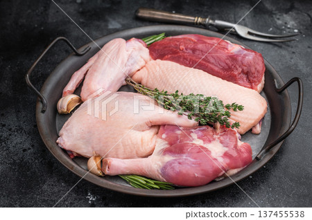 Raw duck parts breast wing thigh and fillet with herbs and garlic in metal pan on dark stone background with fork ideal for poultry stock images. 137455538