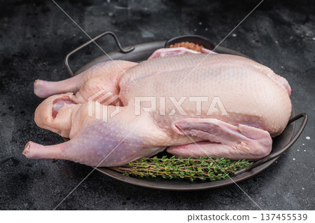 Uncooked duck carcass arranged with herbs and salt in rustic pan against textured dark surface ideal for culinary food photography. 137455539