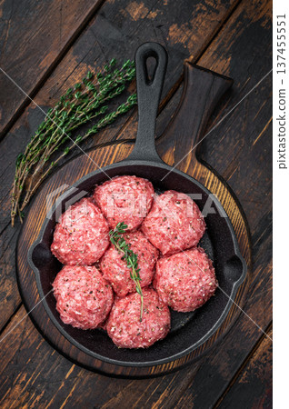 Fresh raw meatballs or Albondiga with thyme in cast iron skillet on rustic wooden background ideal for cooking, protein dishes and food prep themes. Fresh raw meatballs or Albondiga with thyme in cast iron skillet on rustic wooden background ideal for cooking, protein dishes and food prep themes. 137455551