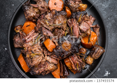 Slow cooked oxtails with vegetables and herbs, hearty comfort food served on dark background, top view Slow cooked oxtails with vegetables and herbs, hearty comfort food served on dark background, top view 137455574