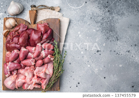 Uncooked chicken liver, hearts, gizzards arranged on weathered board. Speckled grey surface creates modern food photo vibe. Uncooked chicken liver, hearts, gizzards arranged on weathered board. Speckled grey surface creates modern food photo vibe. 137455579