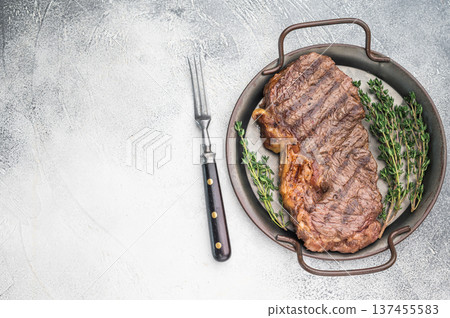 Grilled dry aged striploin steak with thyme on a rustic pan over light textured background cooked to juicy seared perfection. Grilled dry aged striploin steak with thyme on a rustic pan over light textured background cooked to juicy seared perfection. 137455583