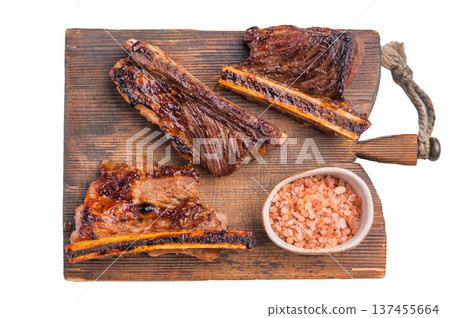 Gourmet grilled beef short ribs served on a rustic wooden board with a bowl of pink Himalayan salt. Clean white background. Gourmet grilled beef short ribs served on a rustic wooden board with a bowl of pink Himalayan salt. Clean white background. 137455664