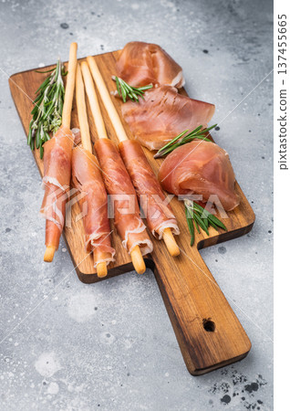 Gourmet Italian Antipasto with prosciutto crudo, grissini breadsticks, and olives on a rustic wooden board. Top view with copy space. 137455665