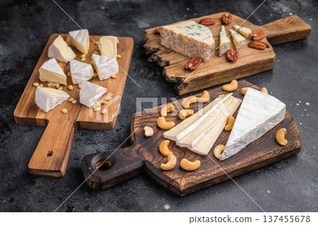 Brie Camembert and Roquefort served on rustic wooden boards with mixed nuts placed over a dark artistic background. Brie Camembert and Roquefort served on rustic wooden boards with mixed nuts placed over a dark artistic background. 137455678