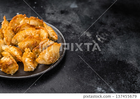 Crunchy gyoza wonton dumplings on dark stone background savory Asian dish with golden crust and sesame garnish Crunchy gyoza wonton dumplings on dark stone background savory Asian dish with golden crust and sesame garnish 137455679